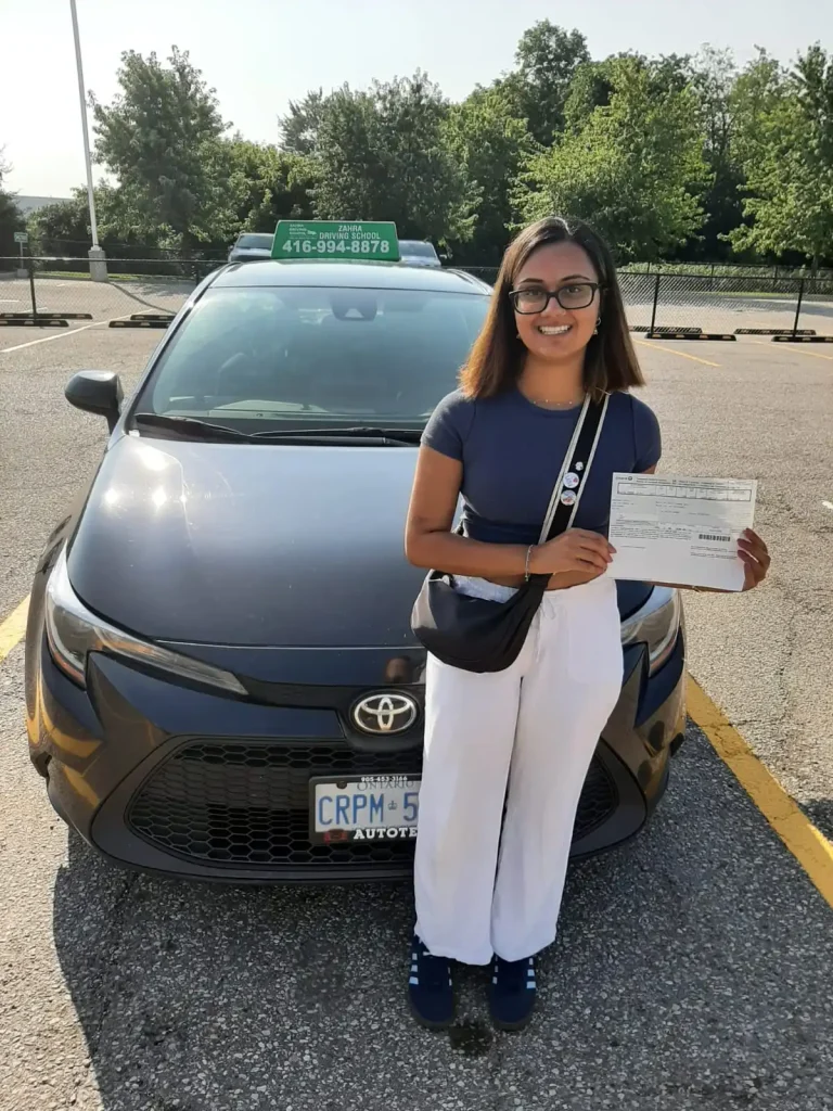 Driving student Vidushi holding her passed G2 test paper next to her instructor inside a Mississauga DriveTest center.