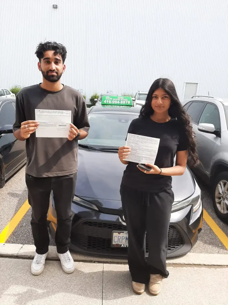 Driving students Emaan and Waleed holding their passed G2 test papers alongside their instructor inside a Mississauga DriveTest center.